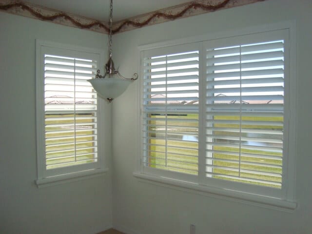 One large window and one small window with white plantation shutters open and overlooking a pond