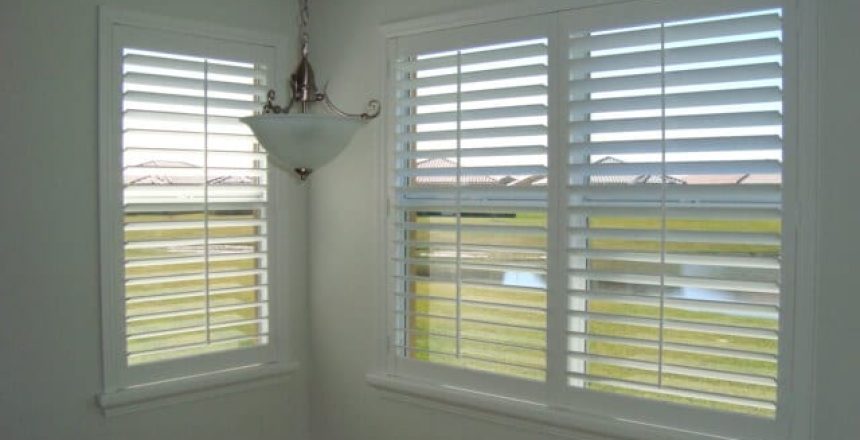 One large window and one small window with white plantation shutters open and overlooking a pond